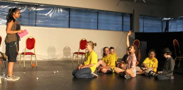 Eine junge Frau gibt einer Gruppe von Kindern Anweisungen auf einer Bühne.