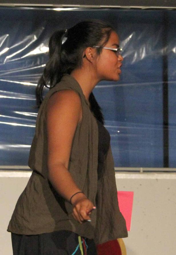 Eine junge Frau mit Brille und Weste spricht vor einem Publikum.