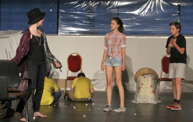 Eine Gruppe von Jugendlichen steht barfuß auf einer Bühne während einer Theateraufführung.