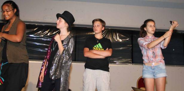 Vier Jugendliche stehen auf einer Bühne, möglicherweise bei einer Aufführung.