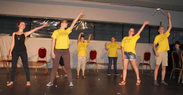 Eine Gruppe junger Leute in gelben T-Shirts tanzt auf einer Bühne.