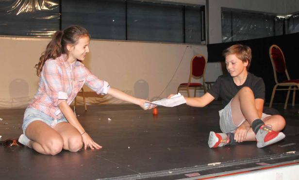 Ein Mädchen übergibt einem Jungen auf einer Bühne ein Blatt Papier.