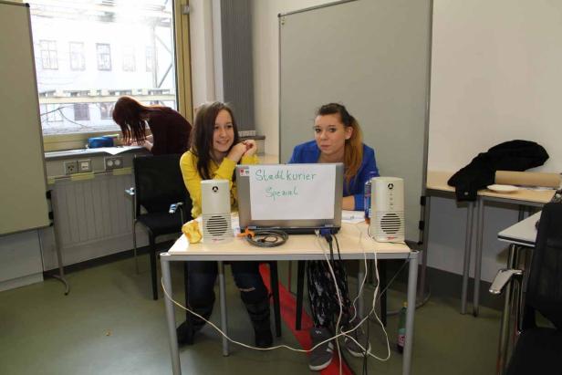 Zwei junge Frauen sitzen an einem Tisch mit einem Laptop, auf dem „Stadtkurier Spezial“ steht.
