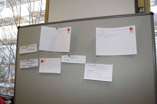 Eine graue Pinnwand mit mehreren Notizen und Zetteln darauf.