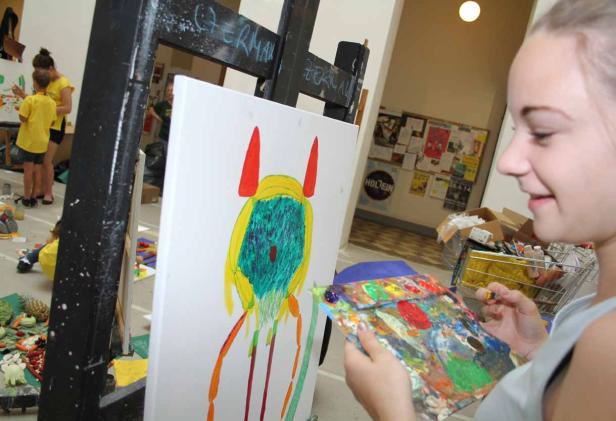 Eine junge Frau malt ein farbenfrohes Monster auf eine Leinwand.