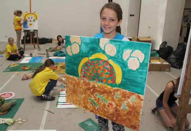 Ein junges Mädchen präsentiert stolz ihr farbenfrohes Gemälde in einem Kunstatelier.