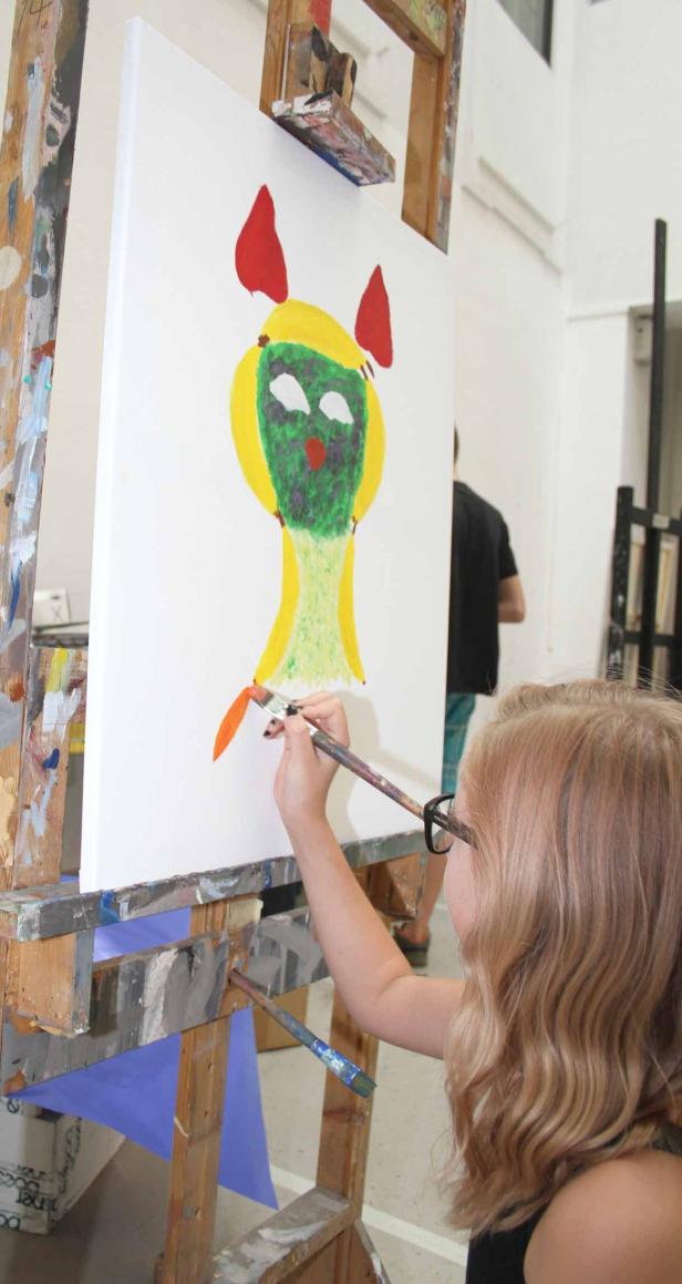 Ein junges Mädchen malt ein fantasievolles Gesicht auf eine Leinwand.