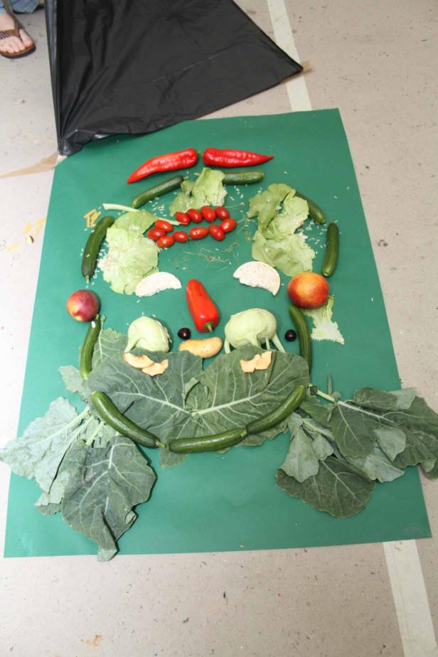 Ein Gesicht aus Gemüse und Obst liegt auf einem grünen Untergrund.