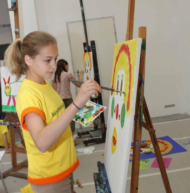 Ein junges Mädchen malt ein buntes Bild auf einer Staffelei.