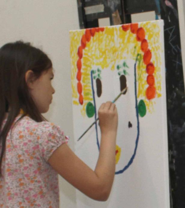 Ein junges Mädchen malt ein farbenfrohes Porträt auf einer Leinwand.