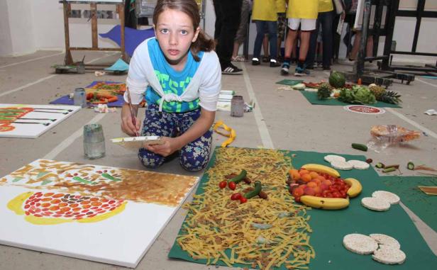 Ein junges Mädchen kniet und malt ein Bild mit Lebensmitteln als Vorlage.