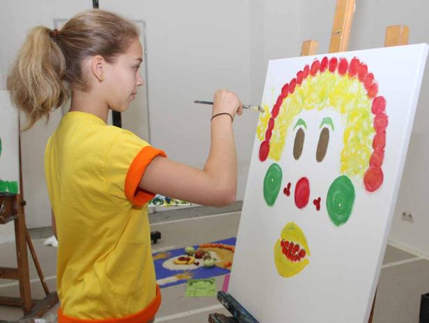 Ein Mädchen malt ein Clown-Gesicht auf eine Leinwand.