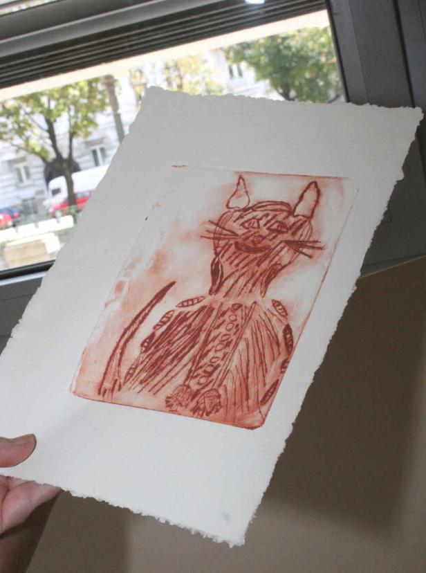 Eine rote Strichzeichnung einer Katze wird vor einem Fenster gehalten.