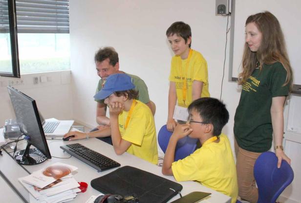 Eine Gruppe von Jugendlichen und ein Erwachsener arbeiten gemeinsam an einem Computer.