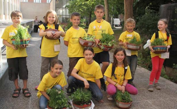 Eine Gruppe Kinder in gelben T-Shirts präsentiert bepflanzte Töpfe.