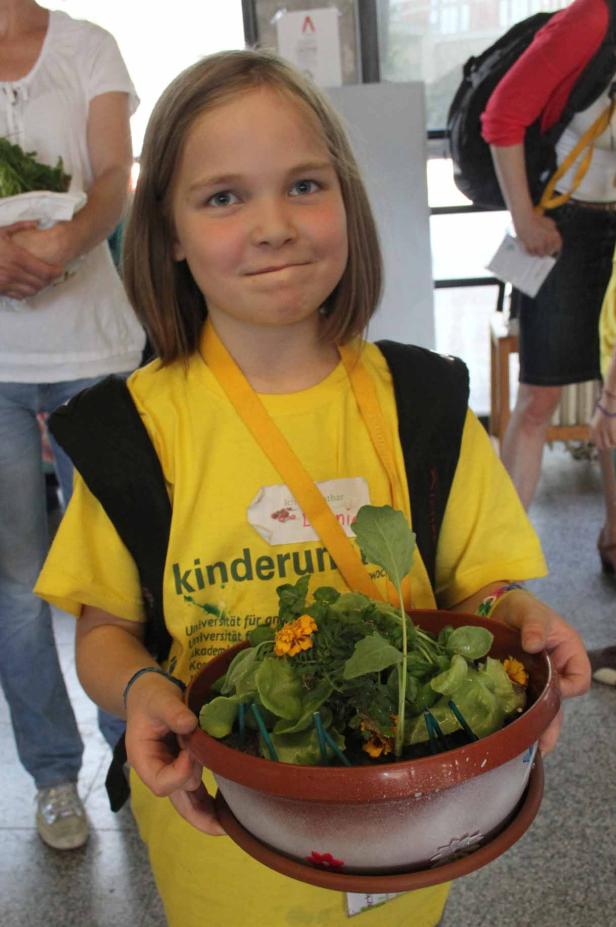 Ein junges Mädchen hält einen Topf mit Salat und Ringelblumen.