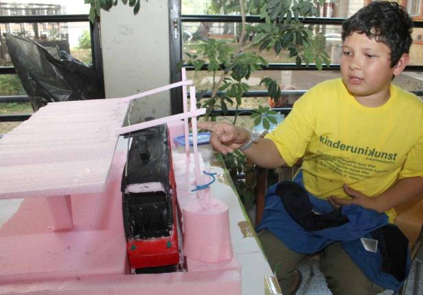 Ein Junge betrachtet ein Modell einer Schwebebahn aus rosa Styropor.