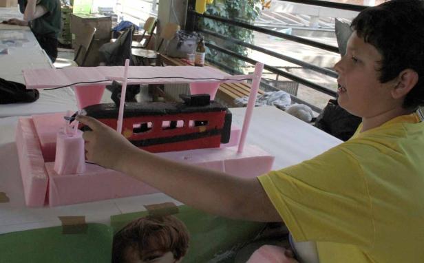 Ein Kind betrachtet ein Modell eines Zuges aus rosa Styropor und rotem Karton.