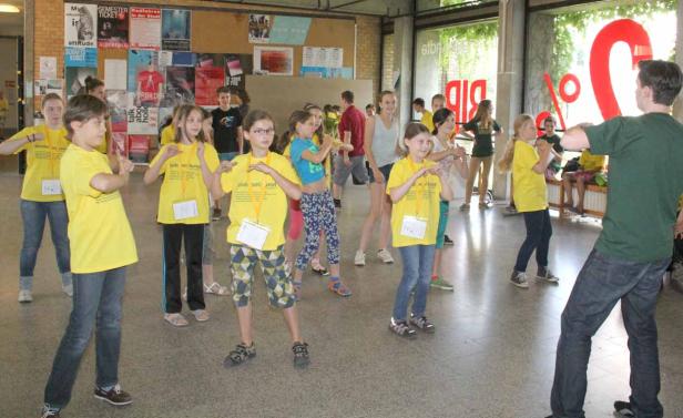 Eine Gruppe Kinder tanzt unter Anleitung eines Mannes in einem Raum.