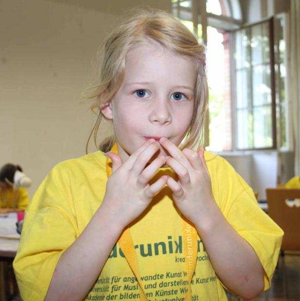 Ein blondes Mädchen in einem gelben T-Shirt berührt ihre Lippen mit den Fingern.
