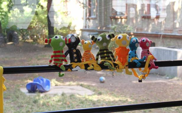 Eine Reihe bunter Stoffpuppen sitzt auf einer Stange vor einem Fenster.