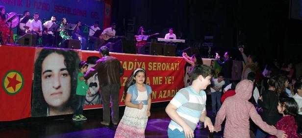 Eine kurdische Musikgruppe spielt auf einer Bühne, während Kinder davor tanzen.