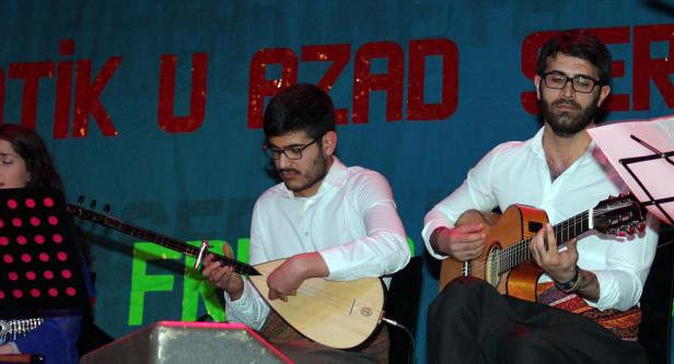 Zwei Männer spielen Gitarre und Saz auf einer Bühne vor einem Banner.