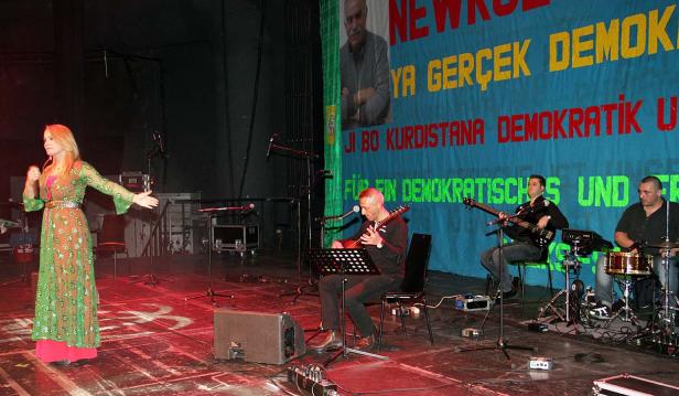 Eine Sängerin tritt mit ihrer Band auf einer Bühne vor einem kurdischen Banner auf.