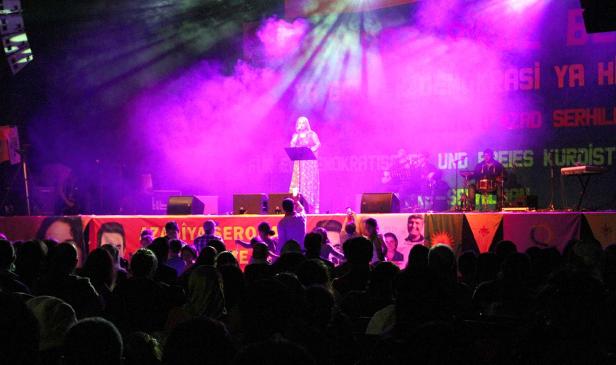 Eine Sängerin tritt vor Publikum auf einer Bühne mit lila Lichteffekten auf.