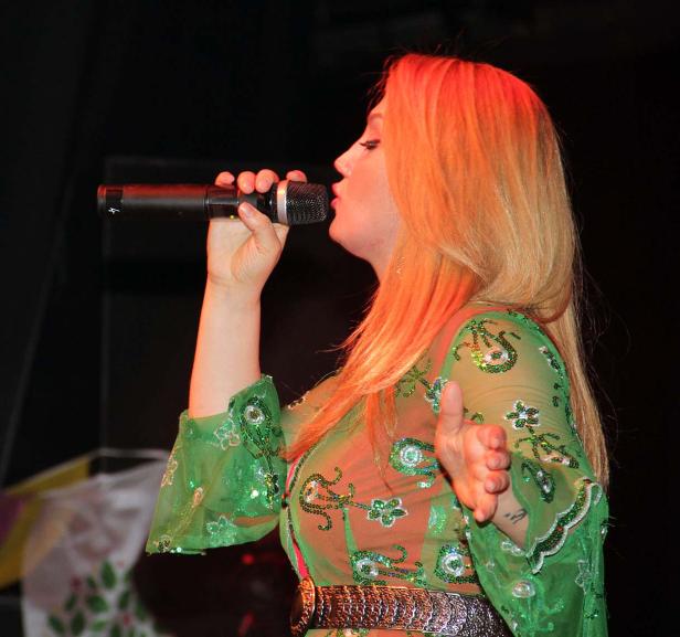 Eine Frau mit blonden Haaren singt in einem grünen, verzierten Kleid in ein Mikrofon.