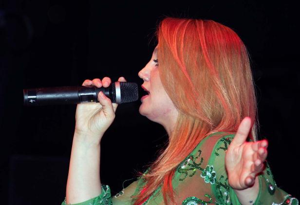 Eine Frau mit roten Haaren singt in ein Mikrofon.