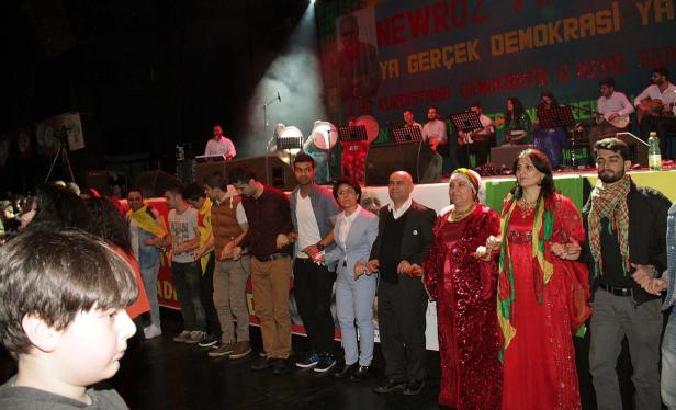 Eine Gruppe von Menschen hält Hände und tanzt vor einer Bühne mit Musikern.