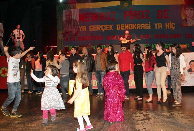 Kinder tanzen auf einer Bühne vor einem Banner mit der Aufschrift „Newroz Piroz Be“.