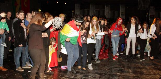 Eine Gruppe von Menschen tanzt gemeinsam, einige mit kurdischen Flaggen geschmückt.