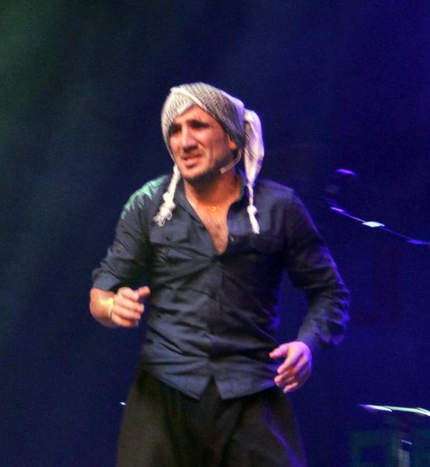 Ein Mann mit einem Tuch auf dem Kopf steht auf einer Bühne.