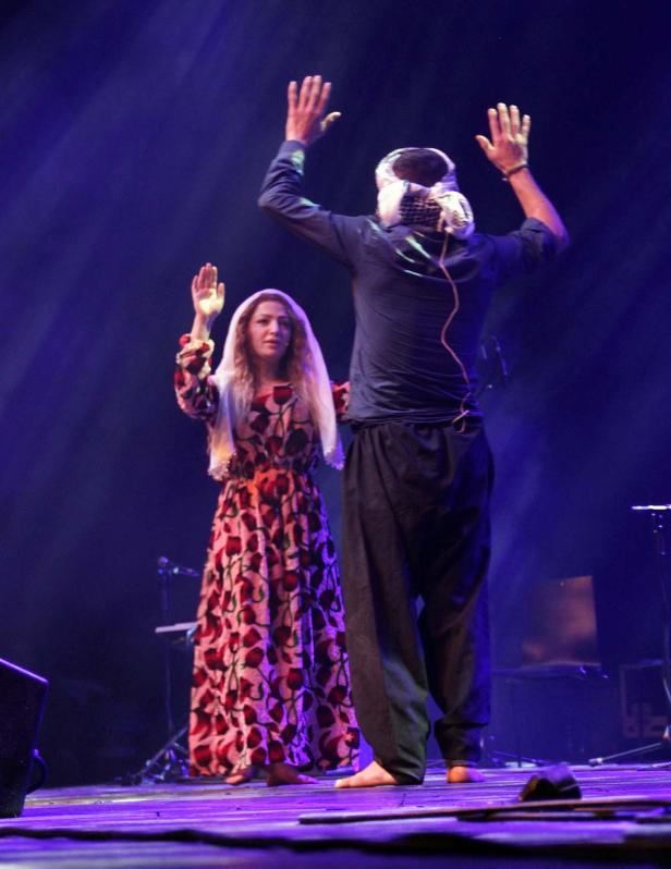 Eine Frau im Kleid und ein Mann tanzen barfuß auf einer Bühne.