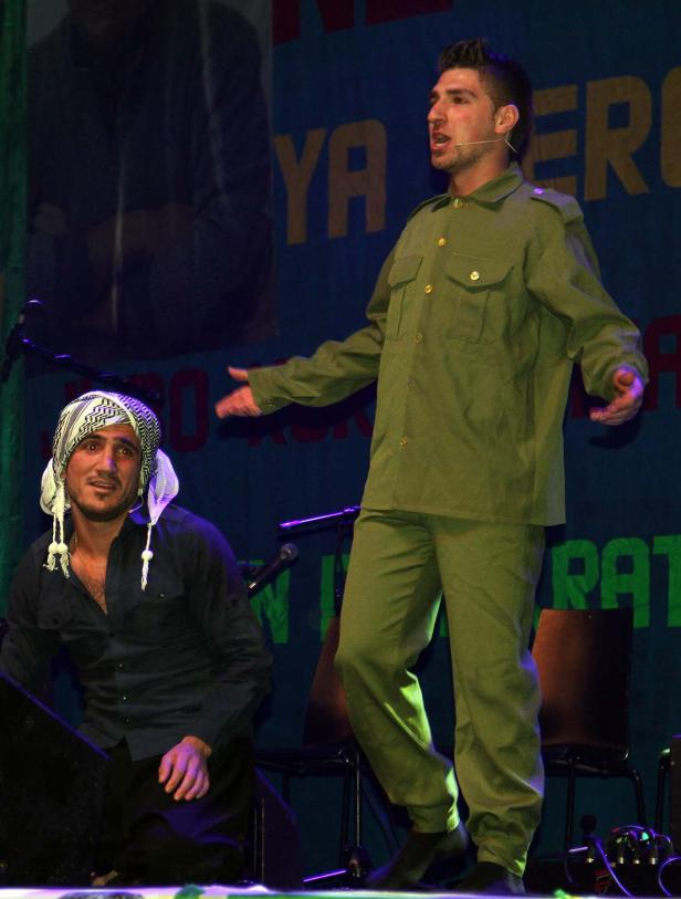 Zwei Männer stehen auf einer Bühne, einer trägt eine Militäruniform.