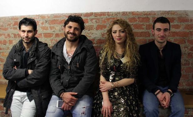 Vier junge Erwachsene sitzen vor einer roten Backsteinmauer.