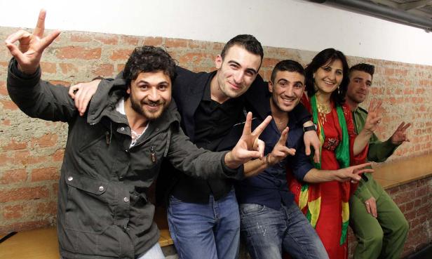 Eine Gruppe von fünf Personen posiert lächelnd vor einer Ziegelwand und zeigt Victory-Zeichen.