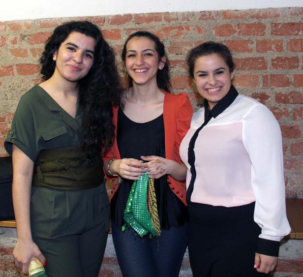 Drei junge Frauen posieren lächelnd vor einer Ziegelwand.