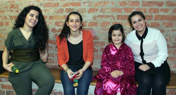 Vier Frauen und ein kleines Mädchen sitzen vor einer roten Backsteinmauer.