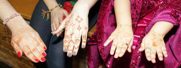 Mehrere Hände mit Henna-Tattoos und bunten Ringen werden gezeigt.