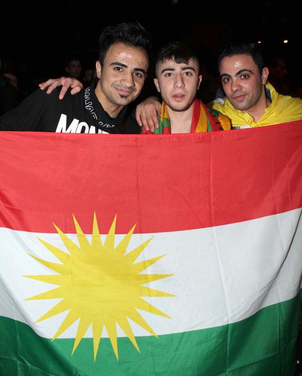 Drei Männer halten eine kurdische Flagge hoch.