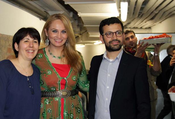 Drei Personen posieren für ein Foto, eine Frau trägt ein verziertes Kleid.