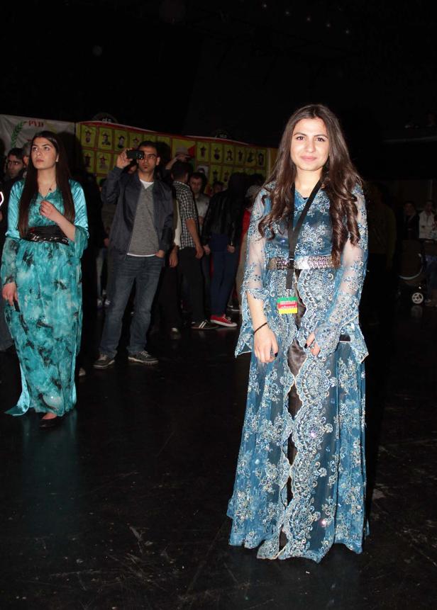 Zwei Frauen in traditionellen kurdischen Kleidern stehen in einem Raum voller Menschen.