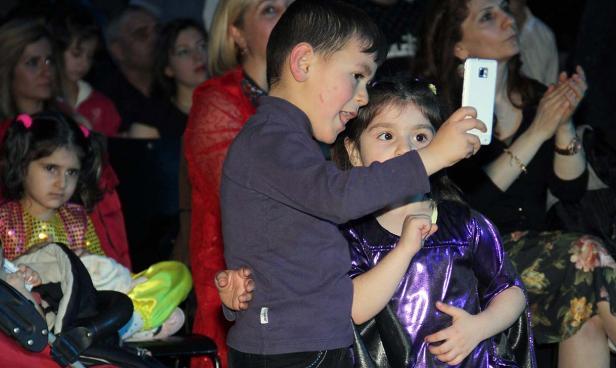 Ein Junge macht mit einem Mädchen ein Selfie vor einer Zuschauermenge.