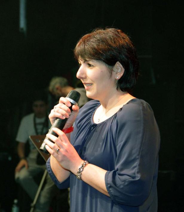 Eine Frau mit dunklen Haaren spricht in ein Mikrofon.