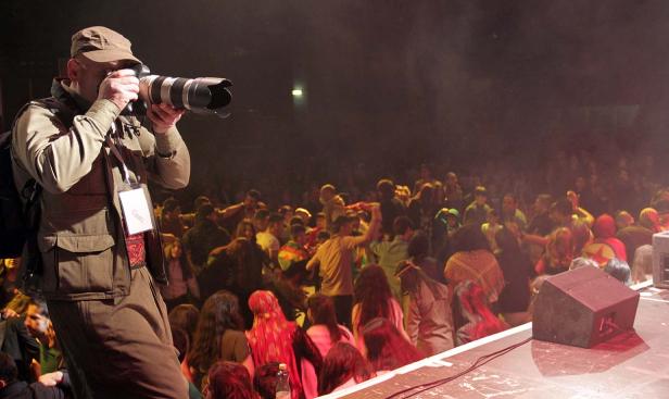 Ein Fotograf steht auf einer Bühne und fotografiert eine Menschenmenge.