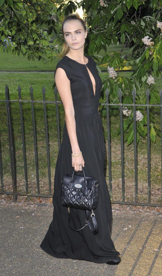 Cara Delevingne trägt ein schwarzes Kleid und eine gesteppte Handtasche.
