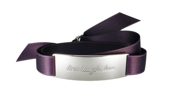 Ein violetter Stoffgürtel mit einer silbernen Schnalle, auf der „live. laugh. love.“ steht.